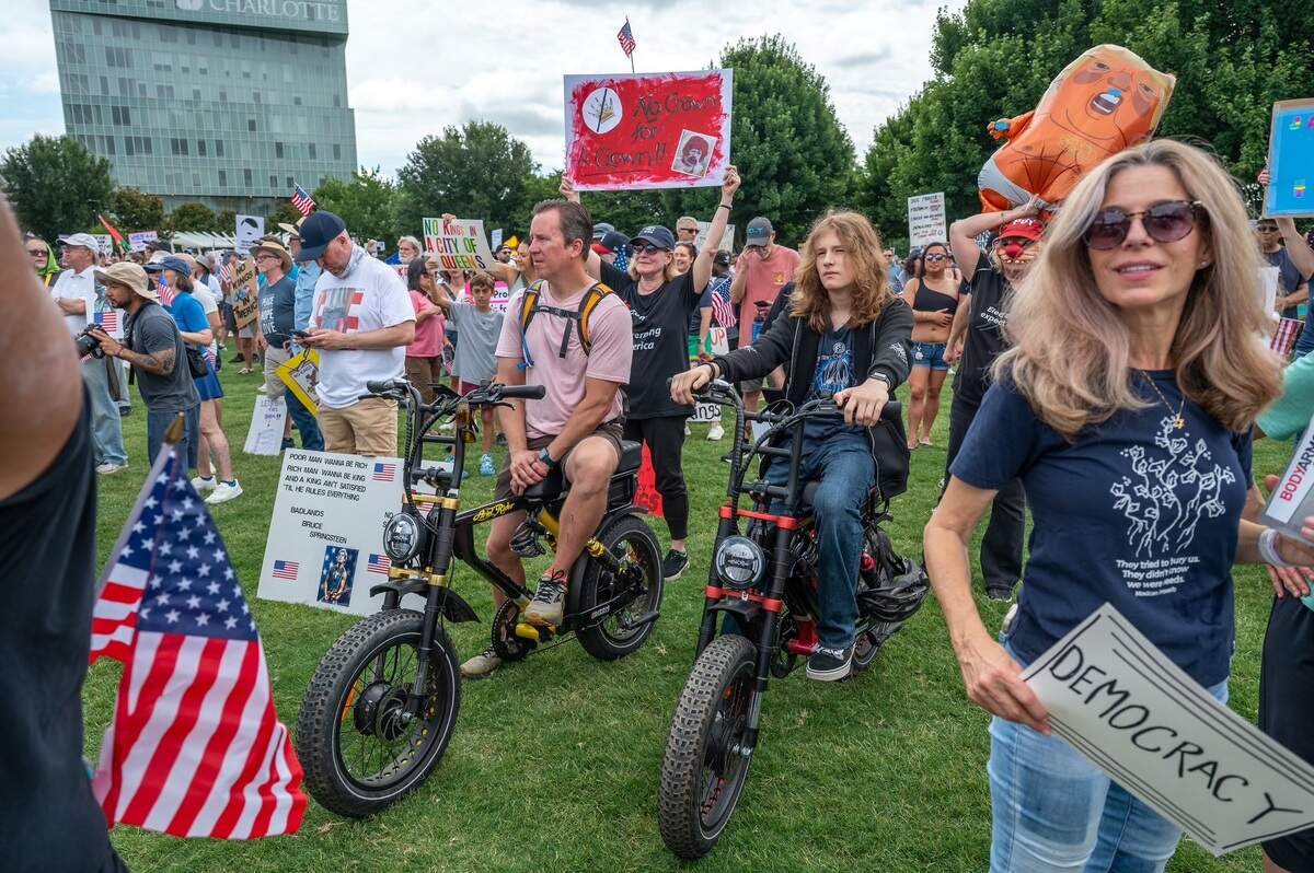 Jeff (left) and Elijah (right) Hartman sit on their motorcycles as they listen to speakers during the No Kings Protest at First Ward Park in Charlotte Saturday, June 14, 2025.