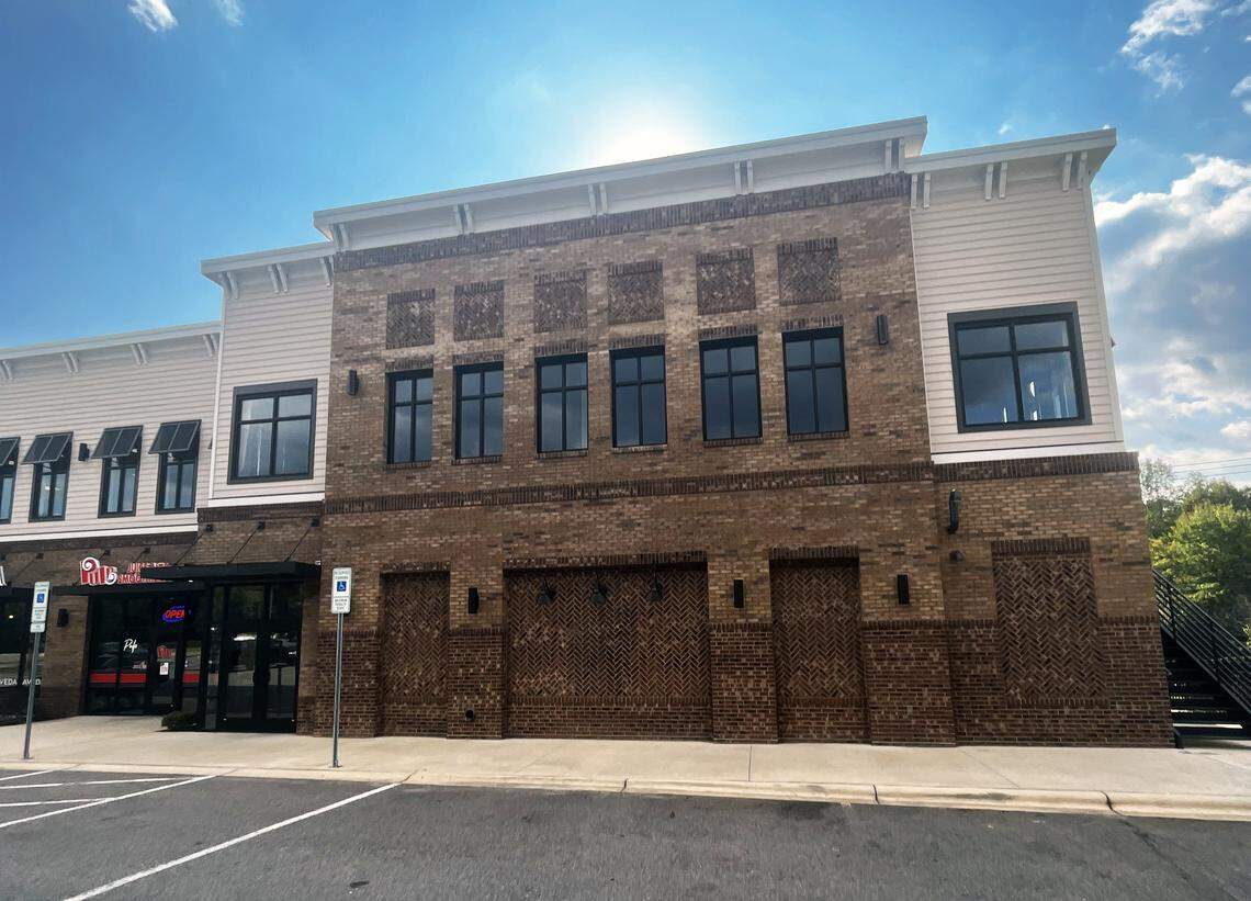 The front exterior of a two-story commercial building with a mix of red brick and light-colored siding, viewed from the parking lot on a sunny day.