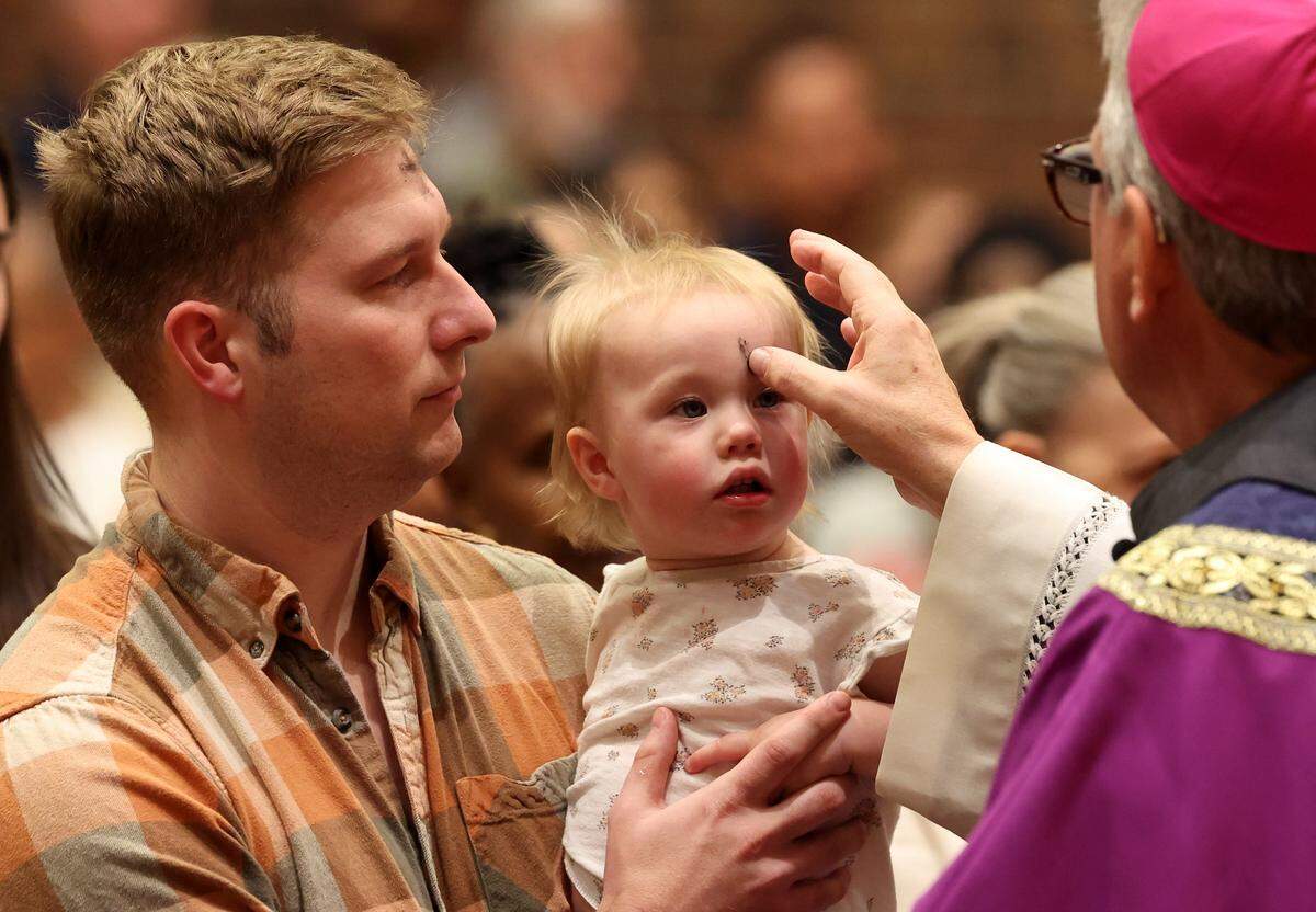 Bishop Michael Martin, right, uses ashes to form the cross on a young child's forehead during an Ash Wednesday Mass at St. John Neumann Catholic Church in Charlotte, NC on Wednesday, February 18, 2026. Bishop Martin is laying out his vision for the church and some of his initial actions have faced scrutiny.