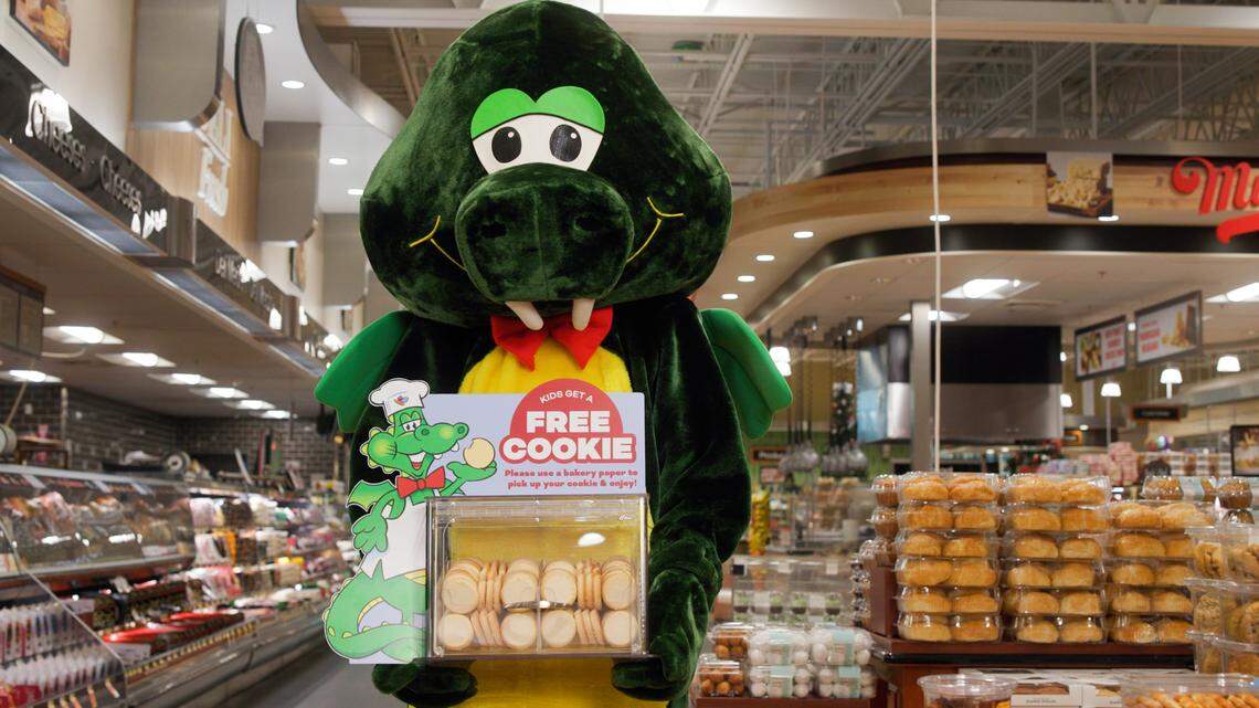Harris Teeter grocery store’s mascot Harry the Happy Dragon holds a cookie display as the tradition of free sugar cookies for kids returns to stores after being cut during the pandemic.