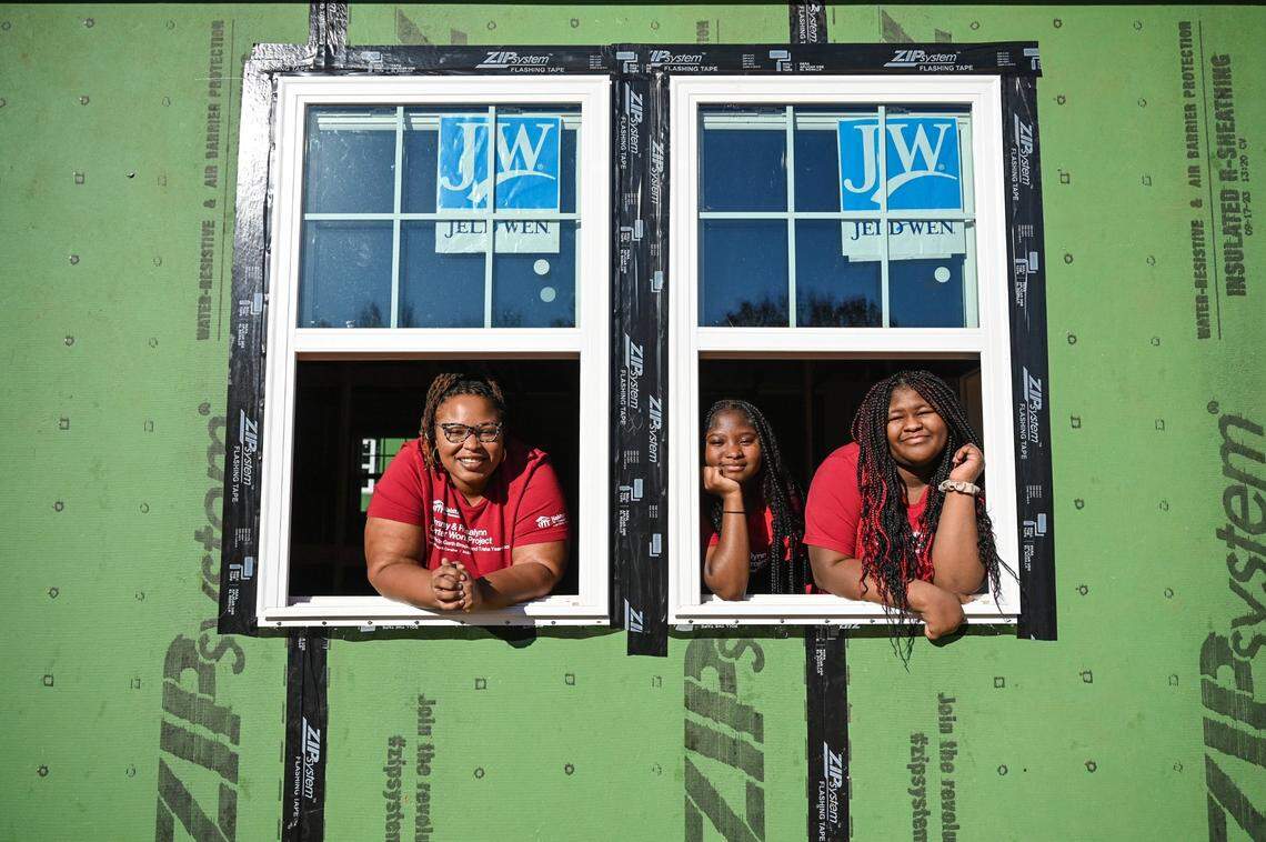 Kee’a Carroll, left, and her daughters Nee’a Tucker, 15, center, and Lee’a Tucker, 14, lean outside the windows to their new home, built during a 27 home Habitat for Humanity build in early October. Carroll is one of a new generation of Habitat For Humanity homeowners and will be moving into the house in the beginning of next year.