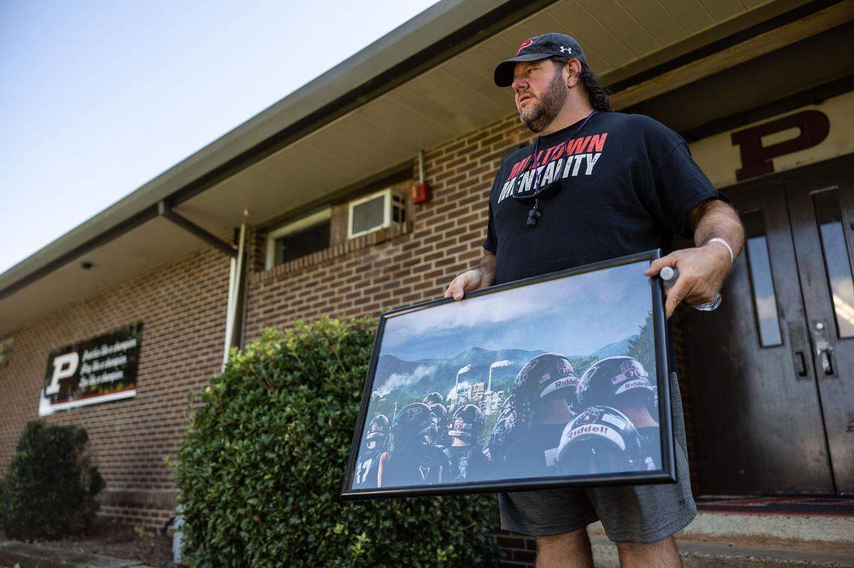 Jody Mathis holds a photo of the football team with the paper mill in the background at Pisgah High School in Canton, N.C., on Tuesday, October 8, 2024.