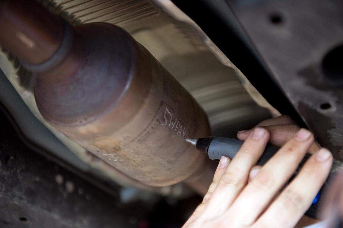 An auto shop employee uses an engraving tool to etch a license plate number on a catalytic converter to prevent theft.