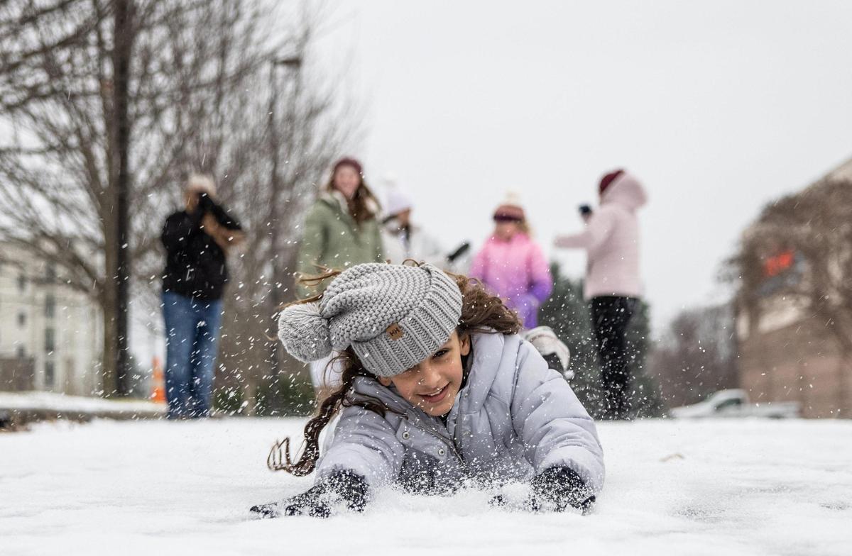 Kylie Fernandez, of Ocala, FL, slides on her belly through the snow in a parking lot during winter storm in Charlotte, N.C., on Sunday, January 16, 2022.
