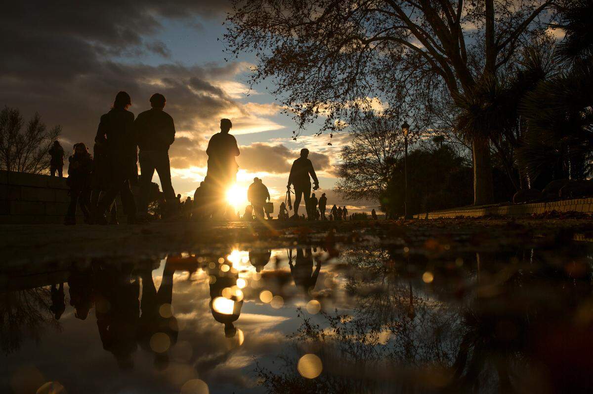 People are reflected in a puddle as they walk along the Temple of Debod public park during sunset in Madrid, Wednesday, Dec. 27, 2017. The park is frequented by locals but also attracts tourists due to its open view at sunset. (AP Photo/Francisco Seco)