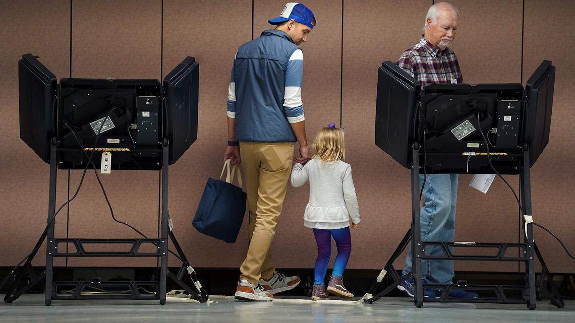 Josh Hughes, left, and daughter, Ellie, 4, are led to a voting machine by precinct official Ed King at Providence United Methodist Church in Charlotte in November. The state Board of Elections approved new touchscreen machines Friday.