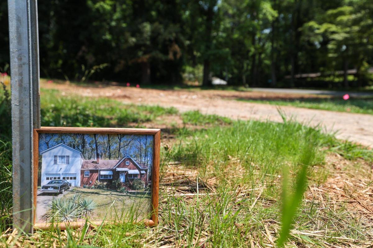 A picture of a house sits in front of an empty lot where the house once stood, on the corner of St. Paul Street and Welch Place.