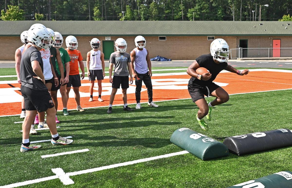 East Lincoln Mustangs running back Chris Daley, right, jumps over pads as his teammates look on during practice at East Lincoln High School in Denver, NC on Monday, July 31, 2023. High school football practices officially began on Monday. East Lincoln was an unbeaten state champion last season and is expected to challenge for another title this season.