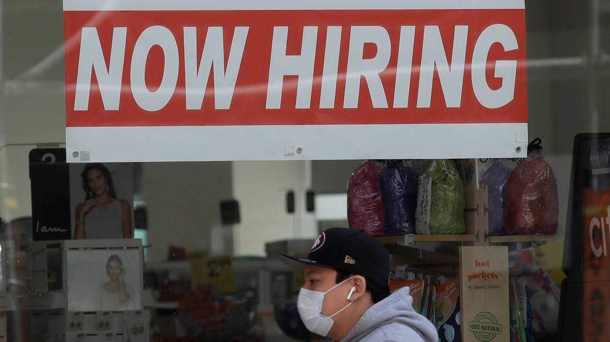 A man wearing a mask walks under a Now Hiring sign in San Francisco. Of the roughly 20 million Americans now receiving some form of unemployment benefits, economists say about half will lose those benefits when two federal programs expire at the end of the year.