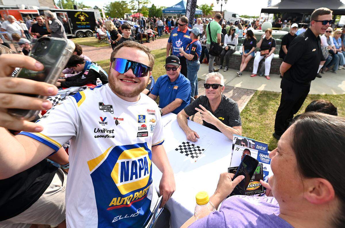 NASCAR fan Zachary Kendall of Laurinburg, NC, left, takes a selfie with former NASCar drivers Ken Schrader and Kenny Wallace, center/background during Thunder Fest in downtown Rockingham, NC on Thursday, April 17, 2025. Fans are celebrating the return of the NASCAR Craftsman Truck Series and XFINITY Series to Rockingham Speedway this weekend.
