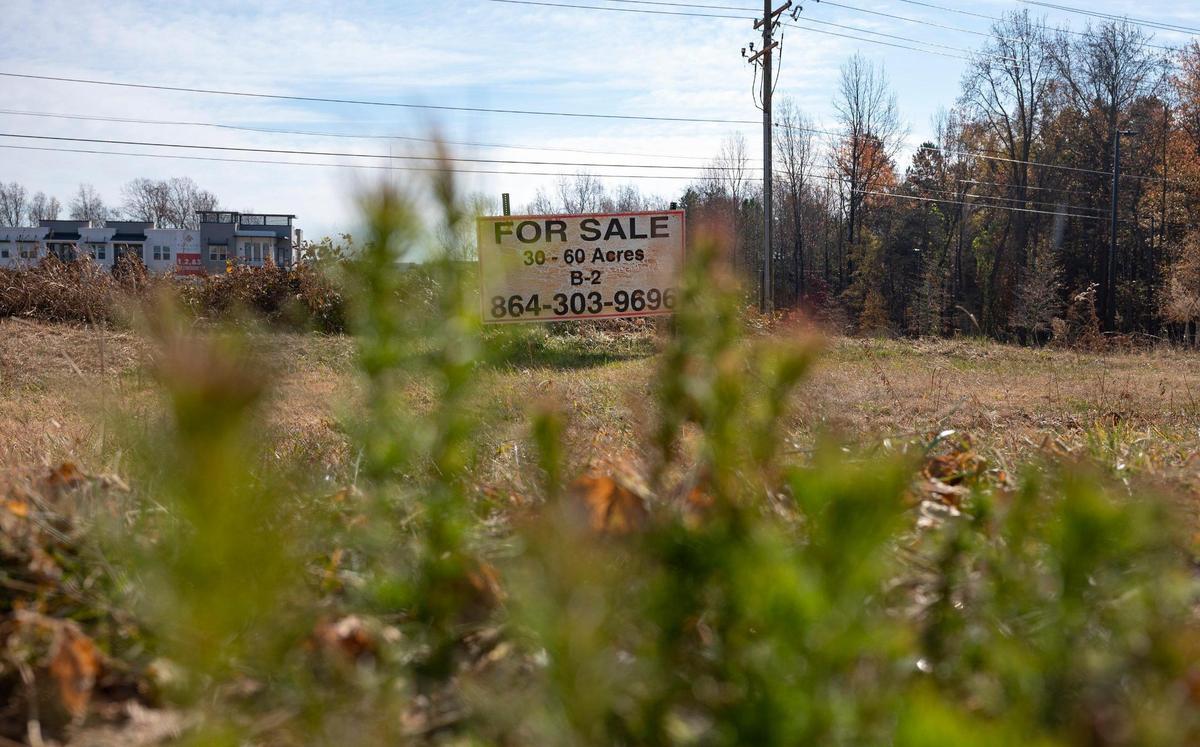 A sign advertising the sale of 30-60 acres of land faces North Tryon Street, across from the University City Boulevard stop on the Lynx Blue Line, on Thursday, December 2, 2021 in Charlotte, NC. The North Carolina tree ordinance guideline for Charlotte states that commercial sites developing for the first time after 2010 will have a fifteen percent tree save requirement that can be satisfied by existing trees providing canopy or by trees planted. Several acres of land that once had several trees have since been cleared for construction of multi-residential apartment complexes, thereby greatly reducing the tree canopy along the light rail’s path.