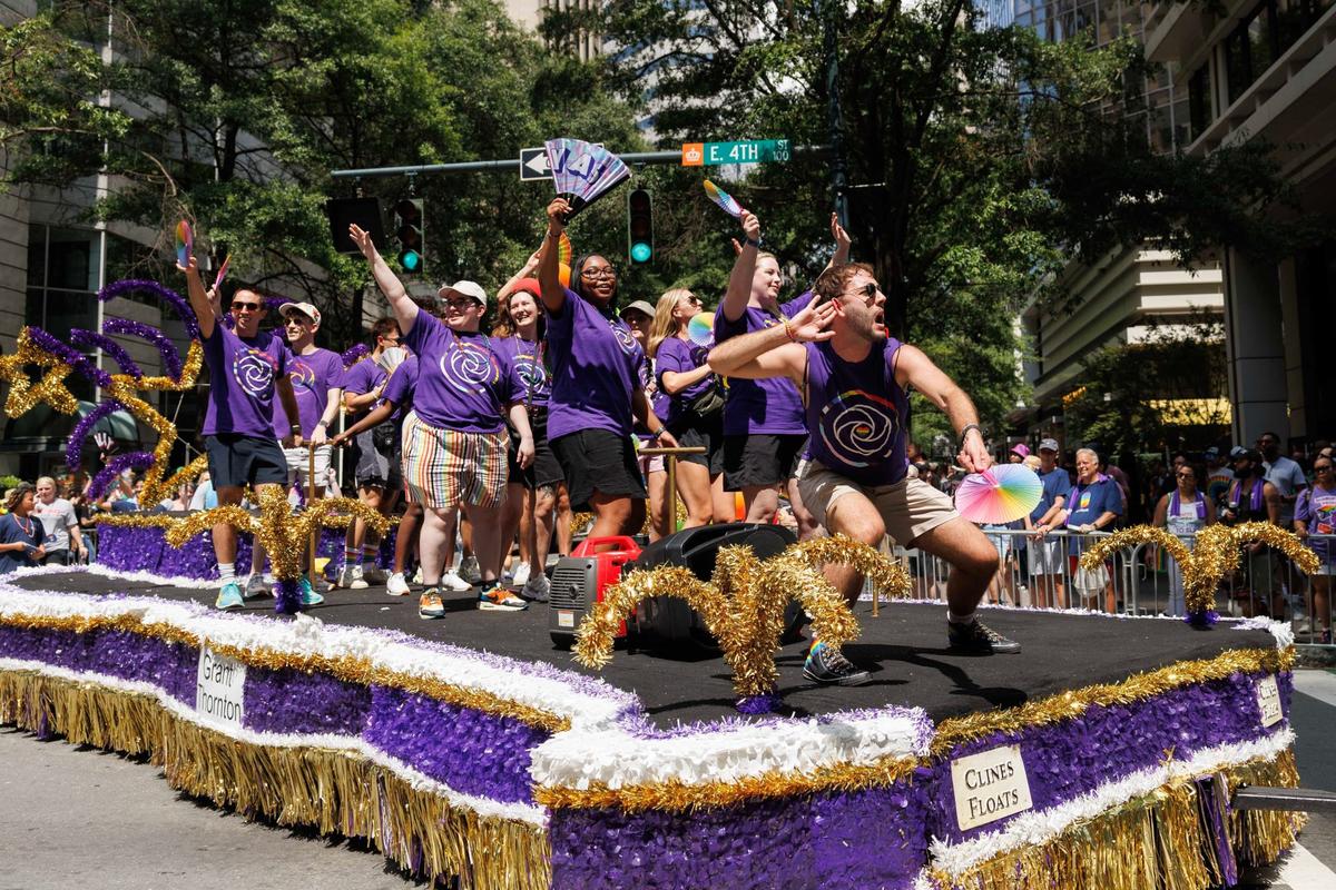 Participants representing Grant Thornton cheer and wave from their float. One member puts a hand to their ear, encouraging the audience to make noise during the Charlotte Pride Festival & Parade on Sunday, Aug. 18, 2024
