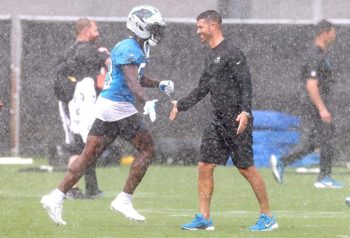 As the rain falls, Carolina Panthers head coach Dave Canales, right, slaps hands with players as they run across the field during the team’s first open workout on Tuesday, May 26, 2026.