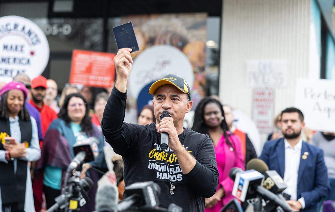 Manolo Betancur holds up his passport and asks who else had to carry their passport on them in case they were stopped by Border Patrol during a press conference at Manolo’s Bakery in Charlotte on Friday.