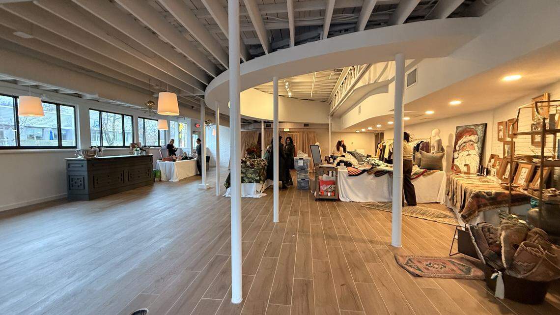Wide-angle interior shot of an event space with white circular columns, wooden floors, large windows, and various vendor tables set up with merchandise.