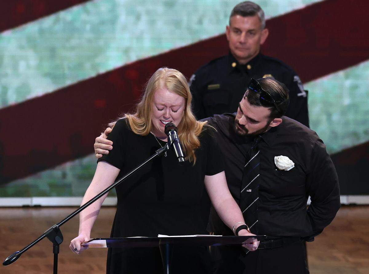 Ashley Eyer, the wife of fallen Charlotte-Mecklenburg Police Officer Joshua Eyer, speaks during her husband’s funeral. At right, Joshua Eyer’s best friend Charlie Sardelli offers support.