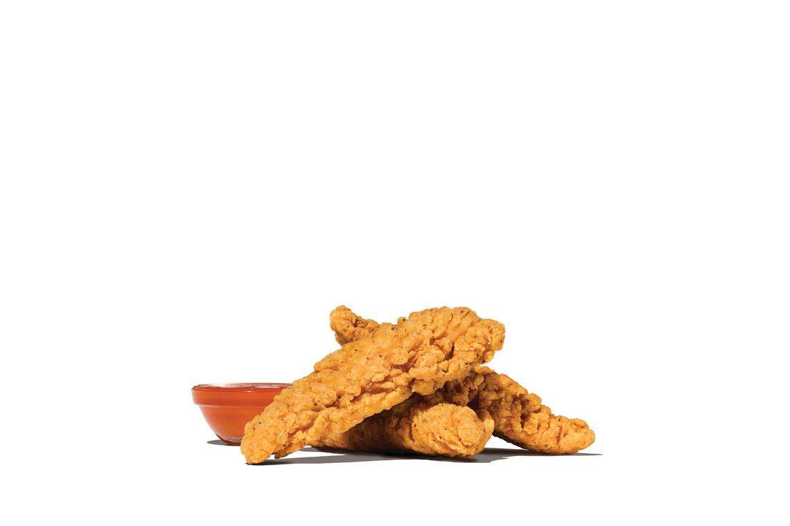 Three breaded, golden-brown chicken tenders are stacked together with a small ramekin of orange-red dipping sauce.