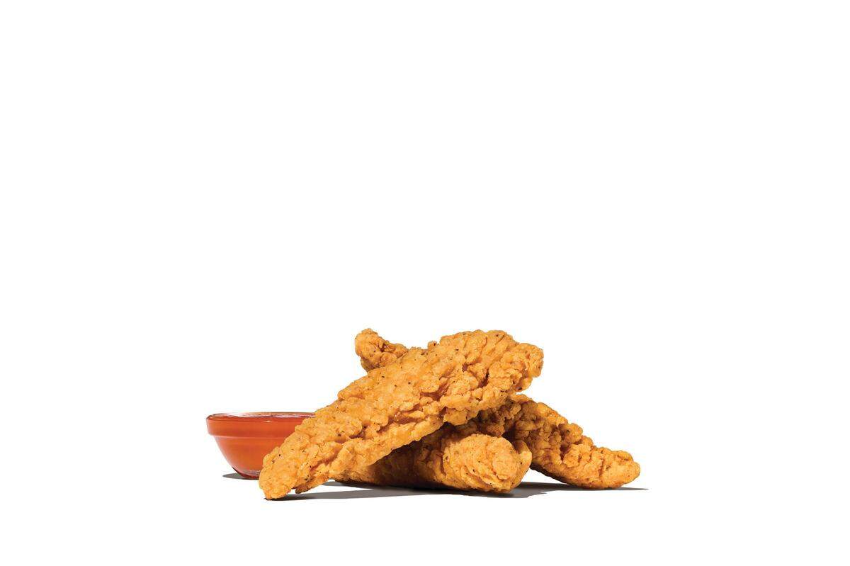 Three breaded, golden-brown chicken tenders are stacked together with a small ramekin of orange-red dipping sauce.