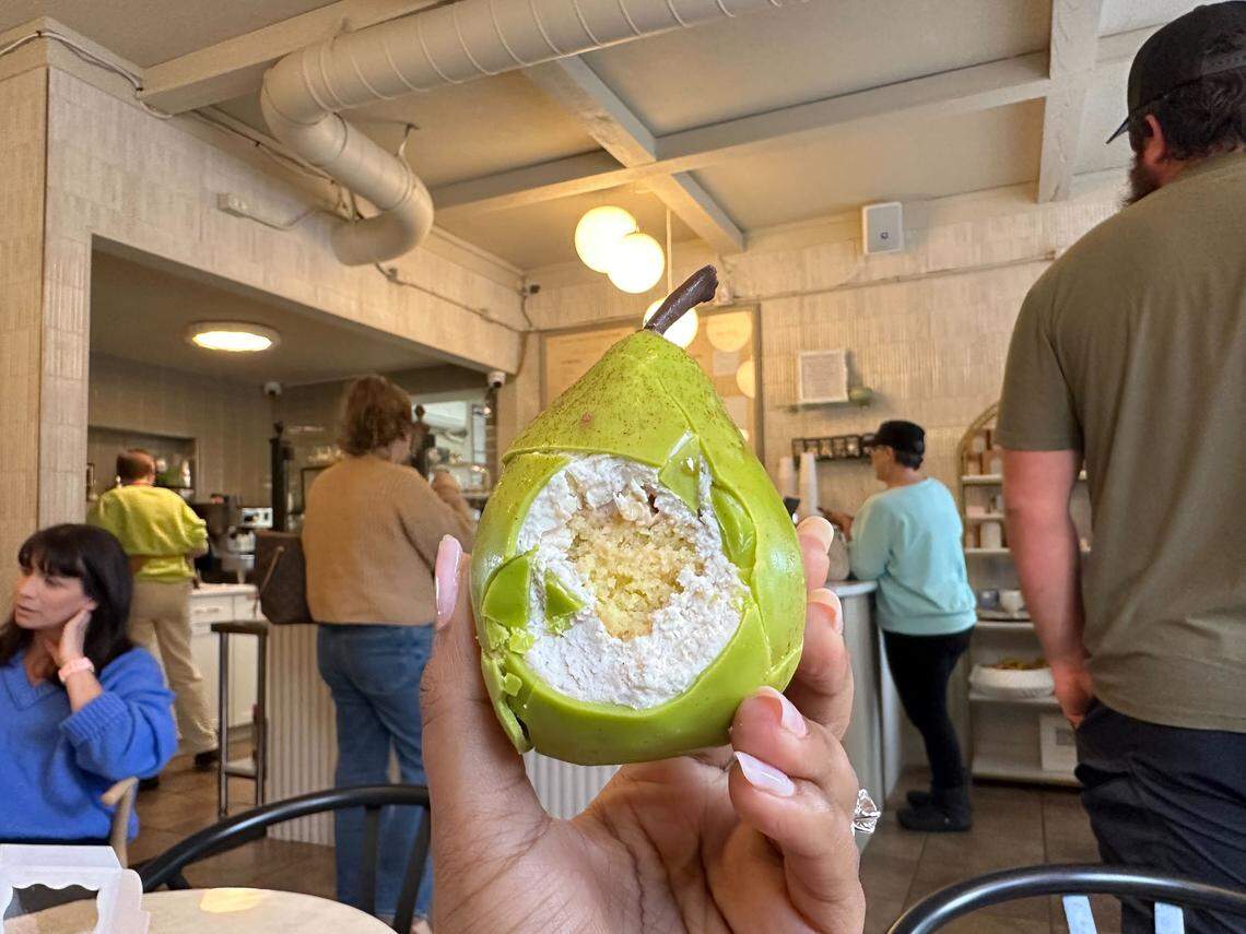 A person’s hand holds the pear-shaped pastry with a large bite taken out, showing the white mousse and yellow cake interior.