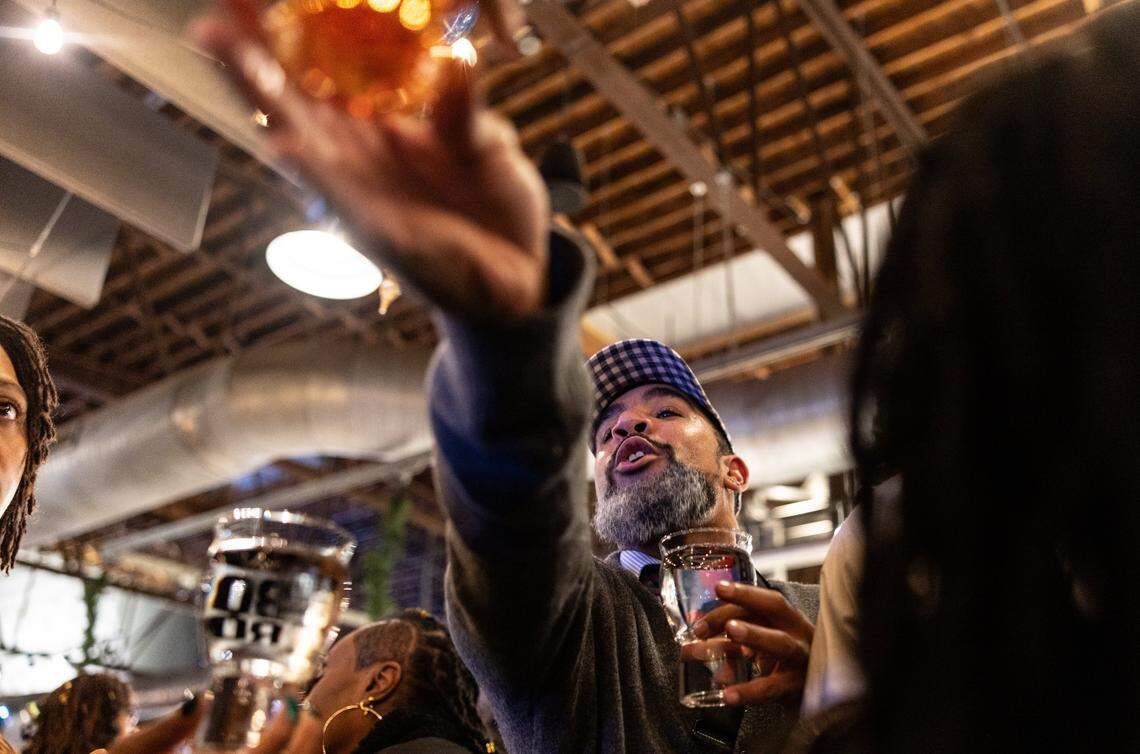 A man reaches across the heads of people to hand someone a drink during the Tall Tour event at Brewers At 4001 Yancey in Charlotte, N.C., on Saturday, December 6, 2025.