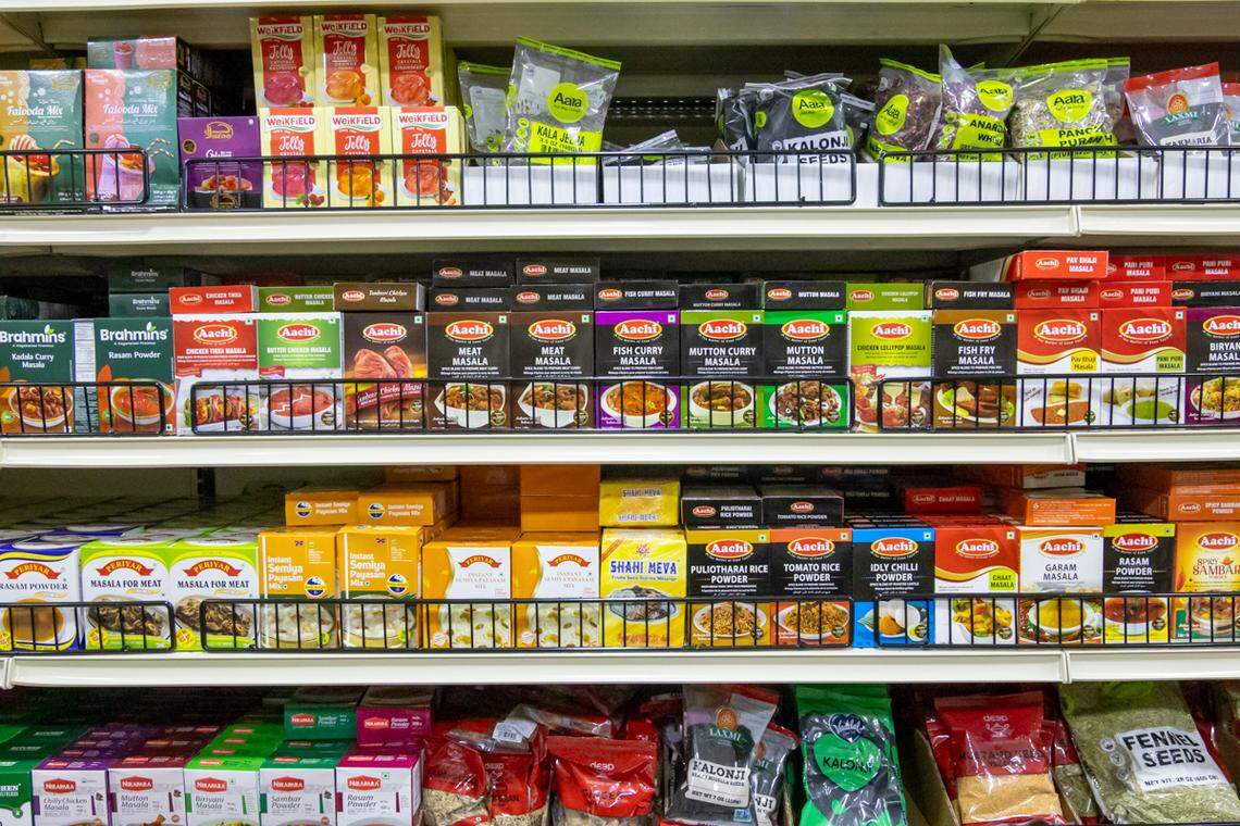 This image is a close-up of a well-stocked supermarket shelf featuring numerous Indian food products. The items include various Aachi brand curry and meat masalas, as well as mixes for dishes like rasam and gulab jamun.