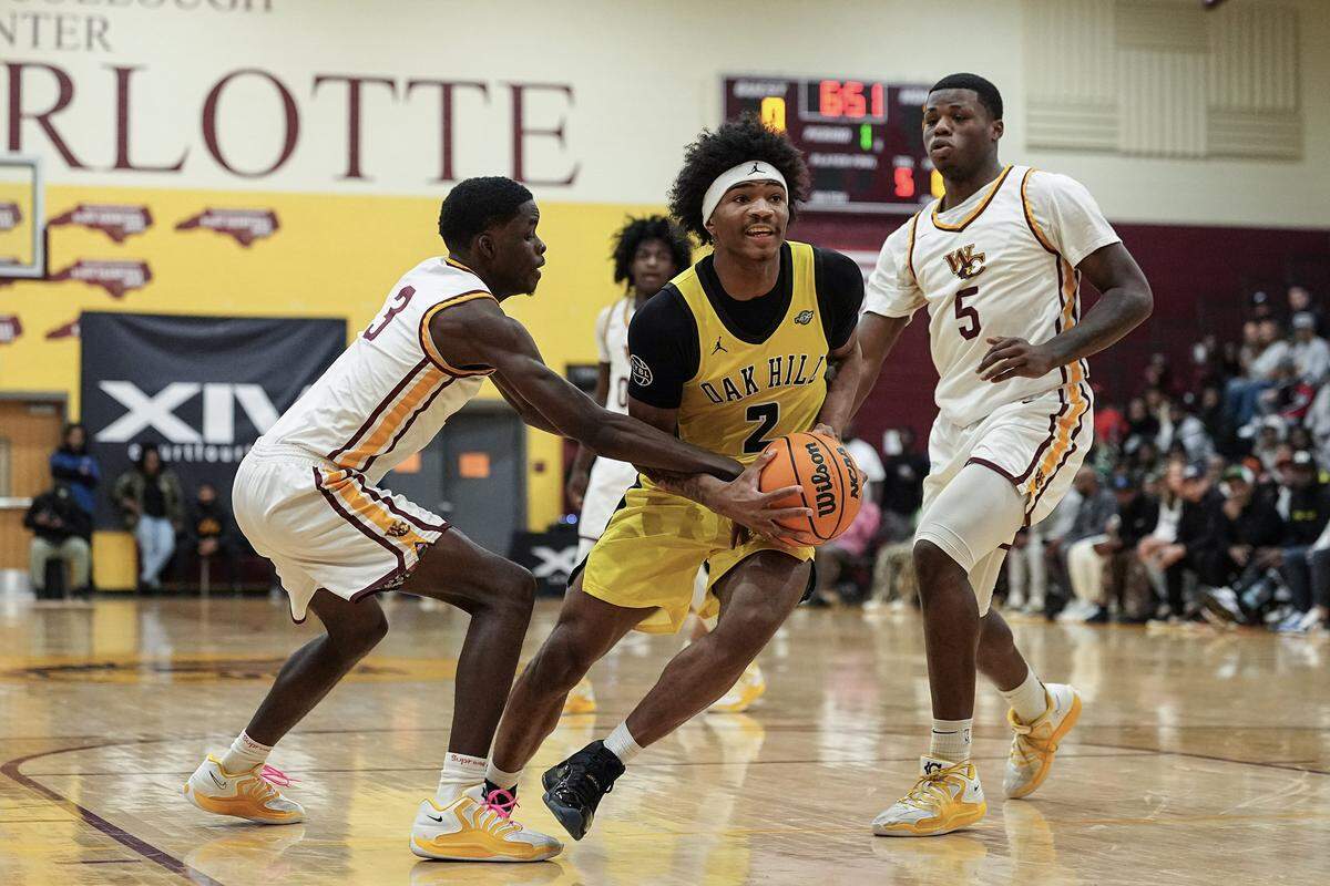 Oak Hill Academy's Korie Corbett (2) drives to the basket between West Charlotte's Amen Ac Pressley (3) and forward Jkhai Wade (5) during the first half of a boys varsity basketball game, Friday, Dec. 19, 2025, in Charlotte, N.C.