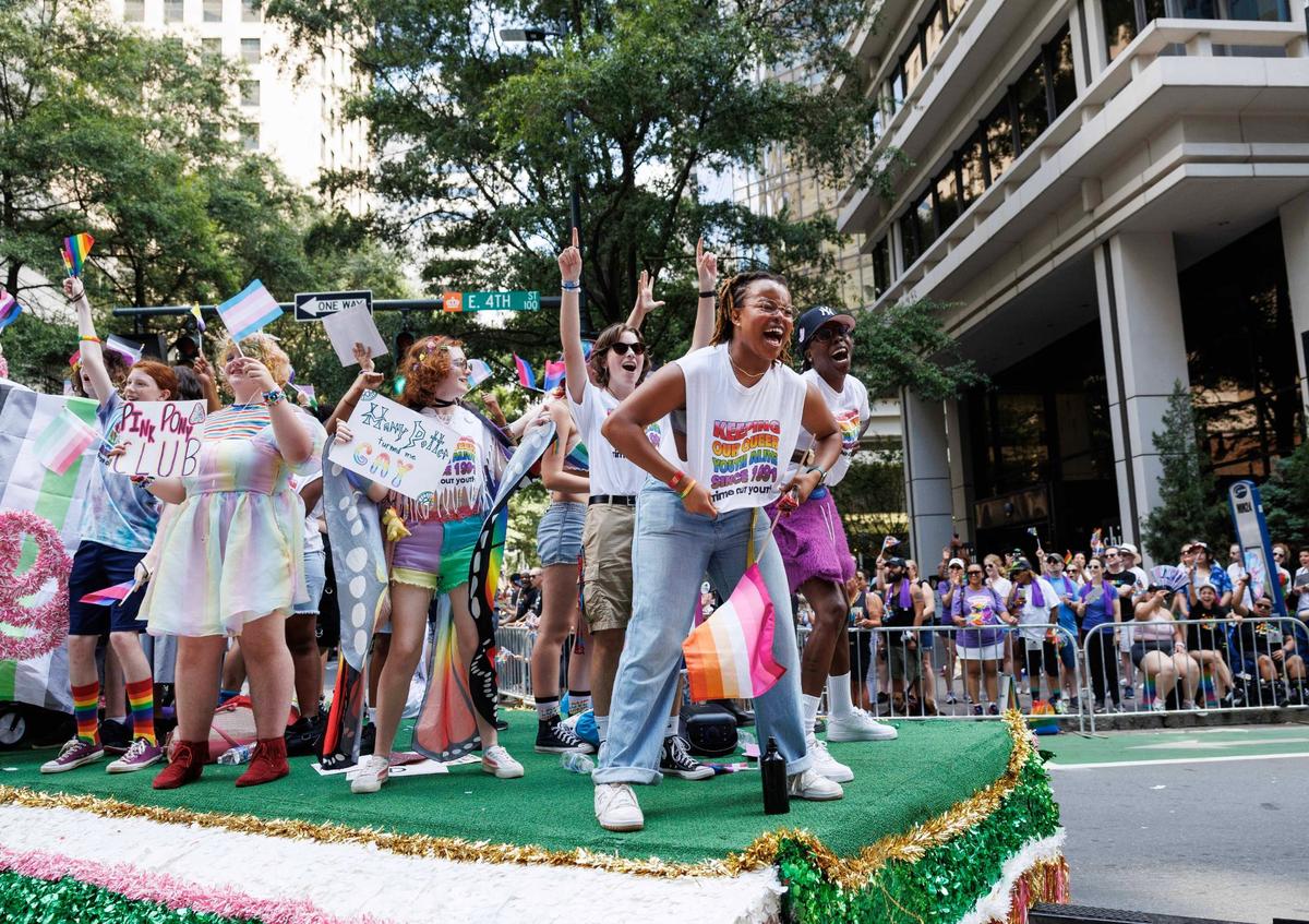 Members of Time Out Youth cheer aboard the organization’s float at the 2024 Charlotte Pride Festival & Parade.. One member holds out their shirt that reads, “Keeping our queer youth alive since 1991.”