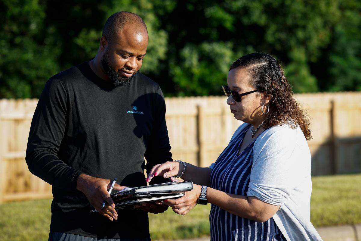 Julie Vidal, right, gets fellow West Charlotte High School parent Thomas Dalton to sign a petition calling on Charlotte Mecklenburg Schools to reinstate head football coach Sam Greiner on Thursday.