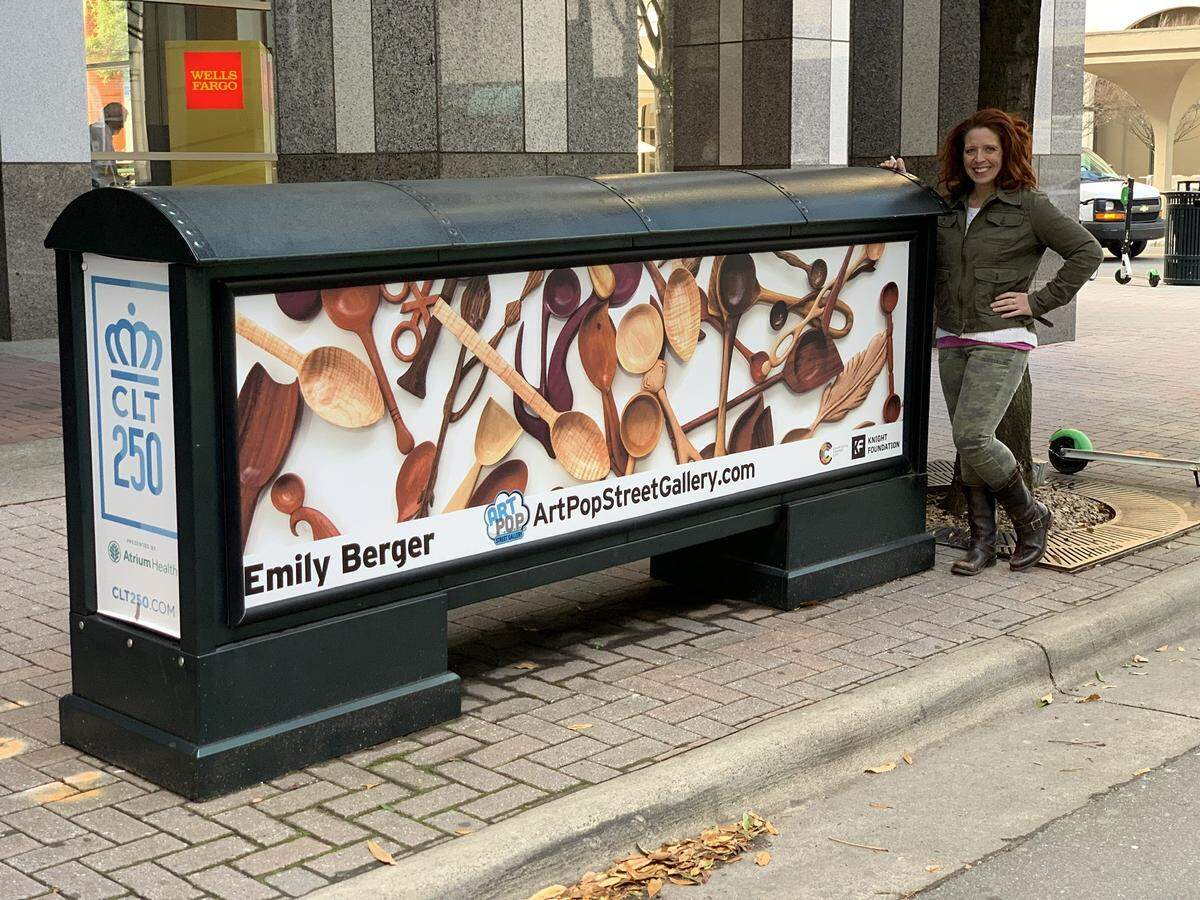 Artist Emily Berger stands next to an ArtPop display of her artwork on a newsstand in uptown Charlotte.