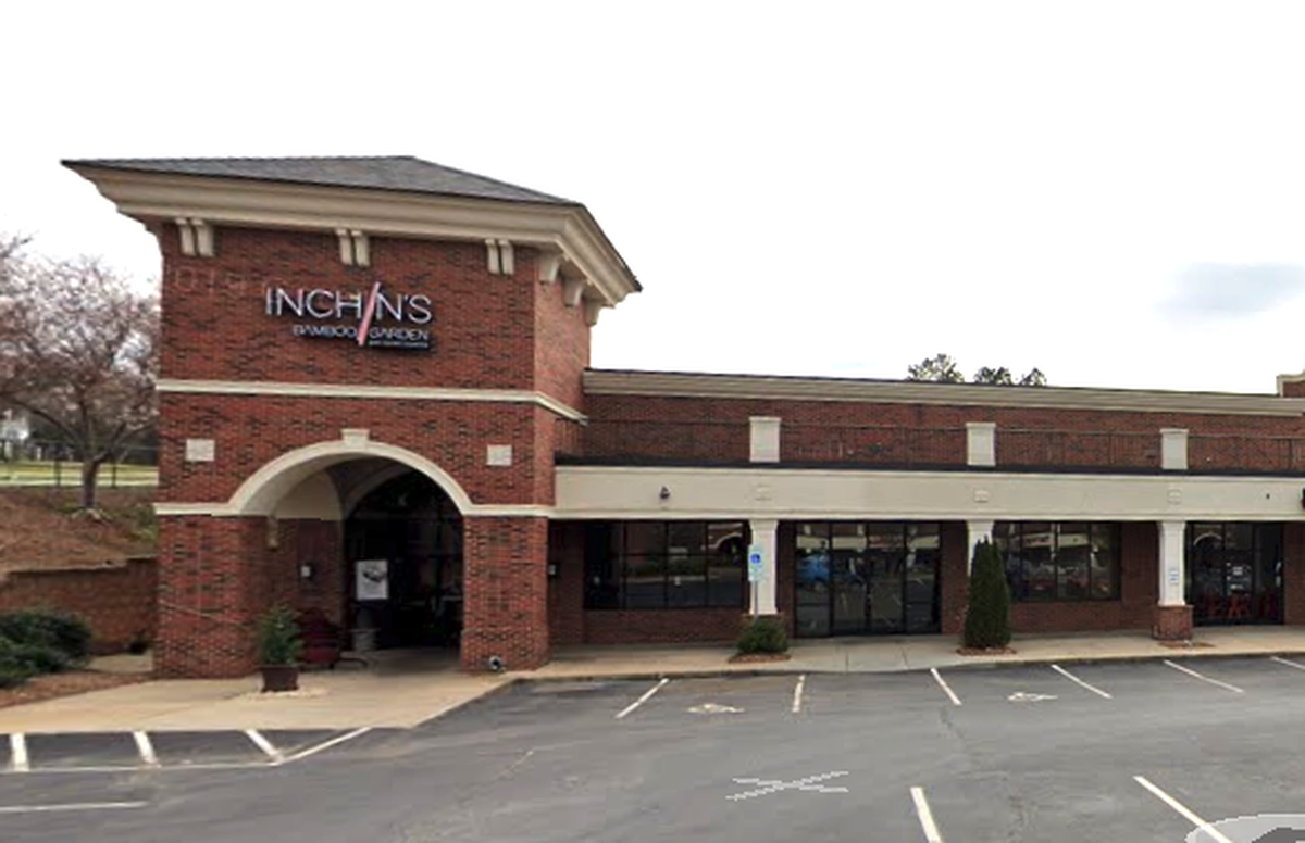 The exterior of the Inchin’s Bamboo Garden restaurant. The building is made of red brick with a prominent corner entrance that has a large archway. A parking lot is in the foreground.