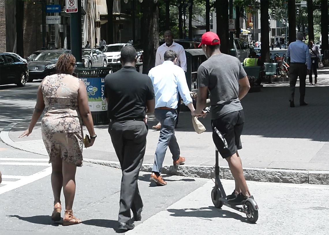 People riding scooters are zipping along Charlotte sidewalks and streets past pedestrians and sometimes in lanes of traffic.
