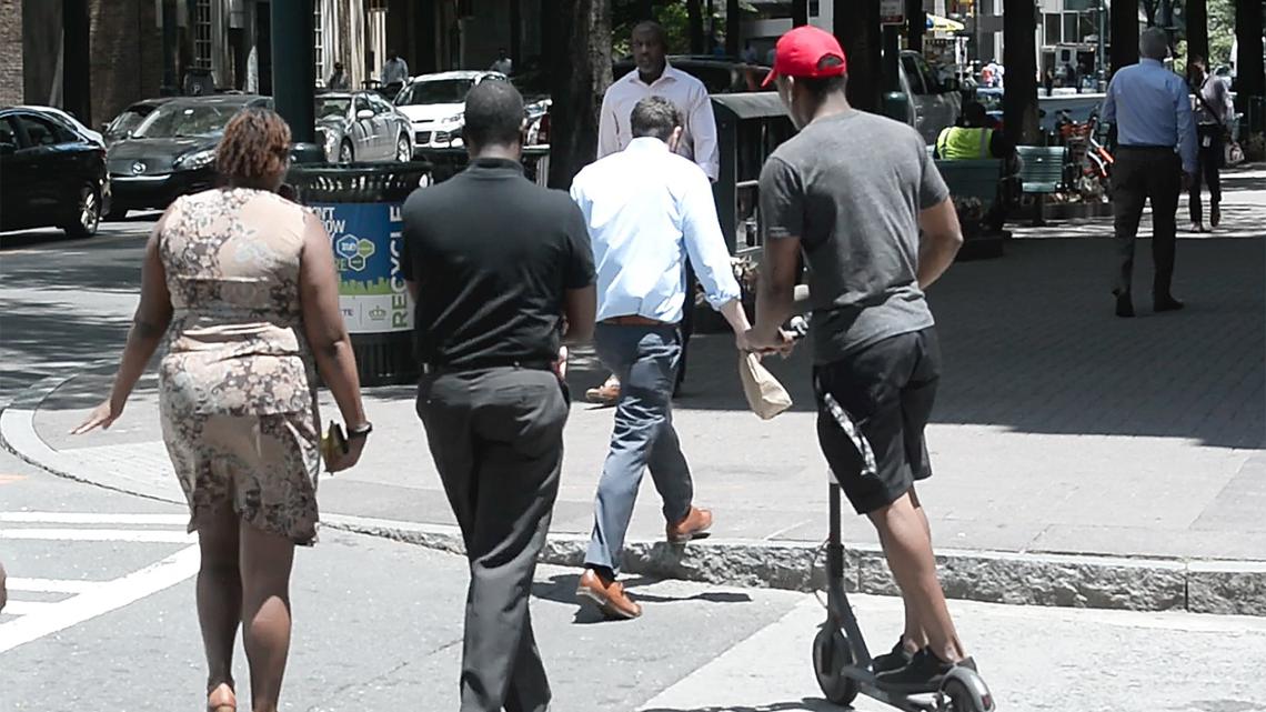 People riding scooters are zipping along Charlotte sidewalks and streets past pedestrians and sometimes in lanes of traffic.