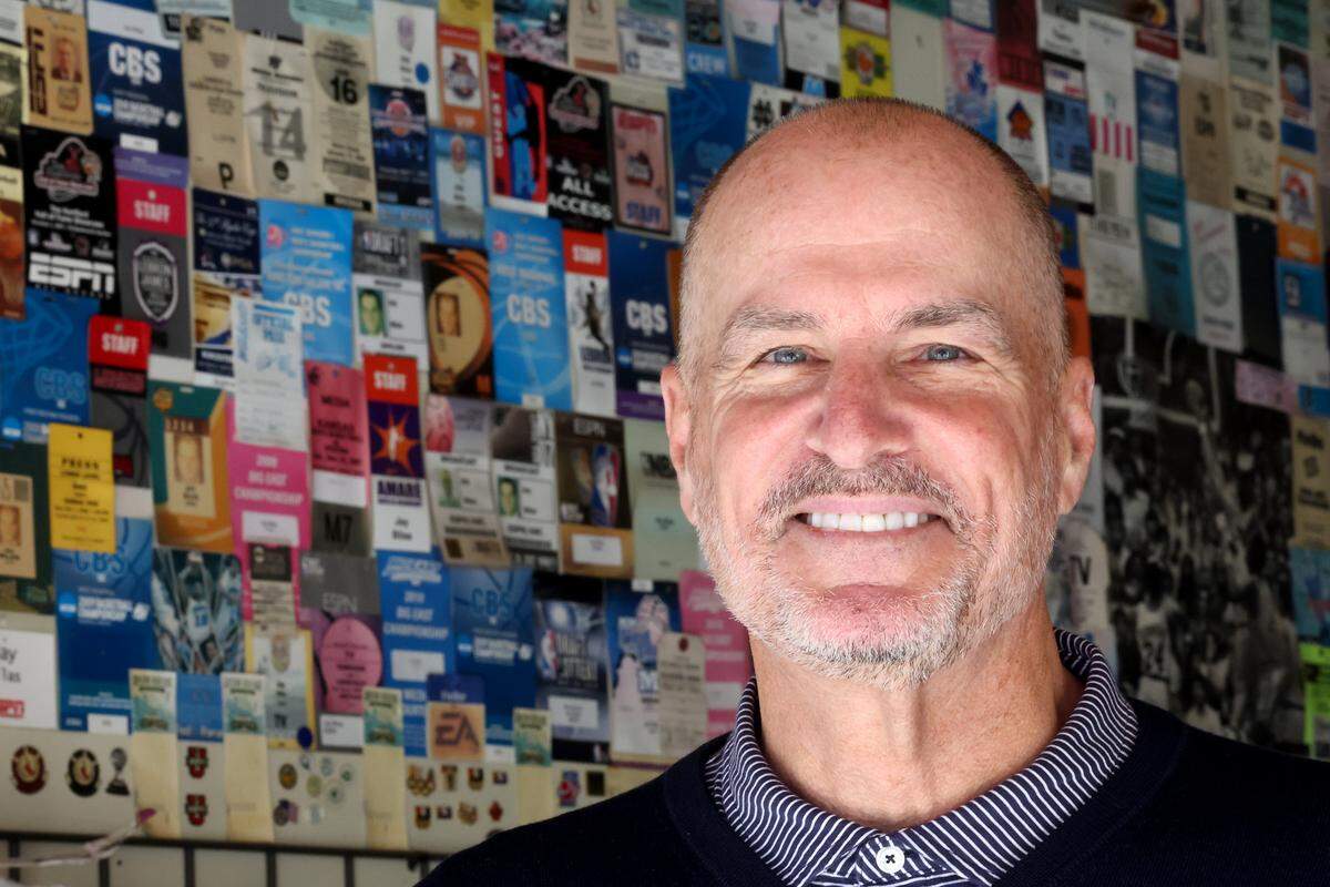 Jay Bilas in front of a wall of old press credentials at his garage in Charlotte.