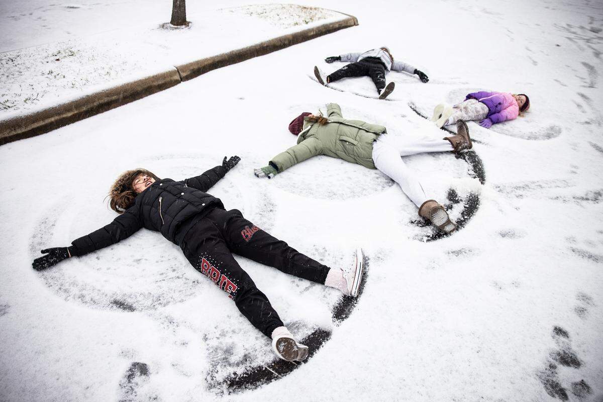 Breille Fernandez, form left, Alexis Collins, Kylie, Fernandez and Faith Collins of Ocala, F., make snow angels in a parking lot during winter storm in Charlotte, N.C., on Sunday, January 16, 2022. They were in town for a cheer competition and normally they don’t get to see any snow.