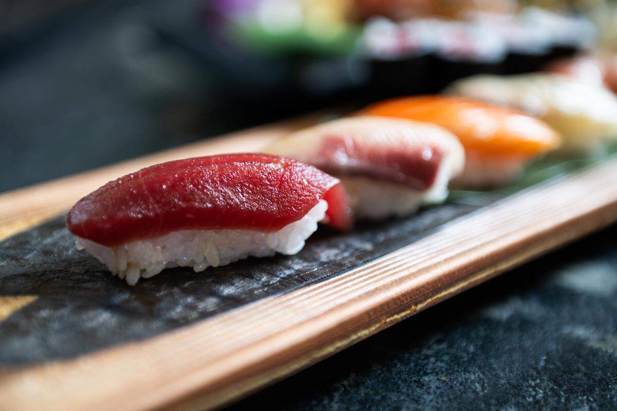 A close-up, selective focus shot of a row of nigiri sushi on a wooden platter, with a piece of red tuna in the foreground.