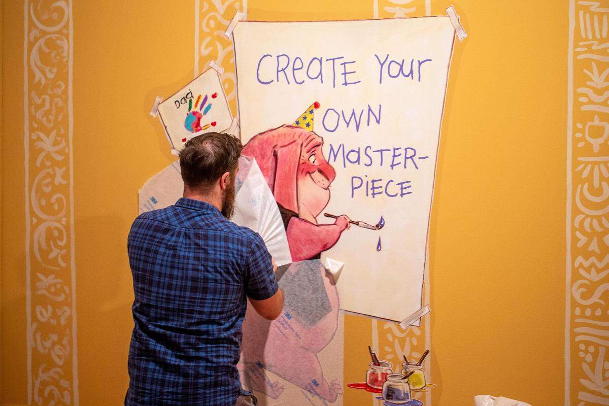 Ian Larson, chief of art services and installation at the Mint Museum, finishes installing a vinyl wrap for the “Never Abandon Imagination: The Fantastical Art of Tony DiTerlizzi” exhibition, which opens June 22. The wrap instructs visitors to draw their own imaginative characters. Visitors may recognize DiTerlizzi’s illustrations from Dungeons & Dragons or The Spiderwick Chronicles.