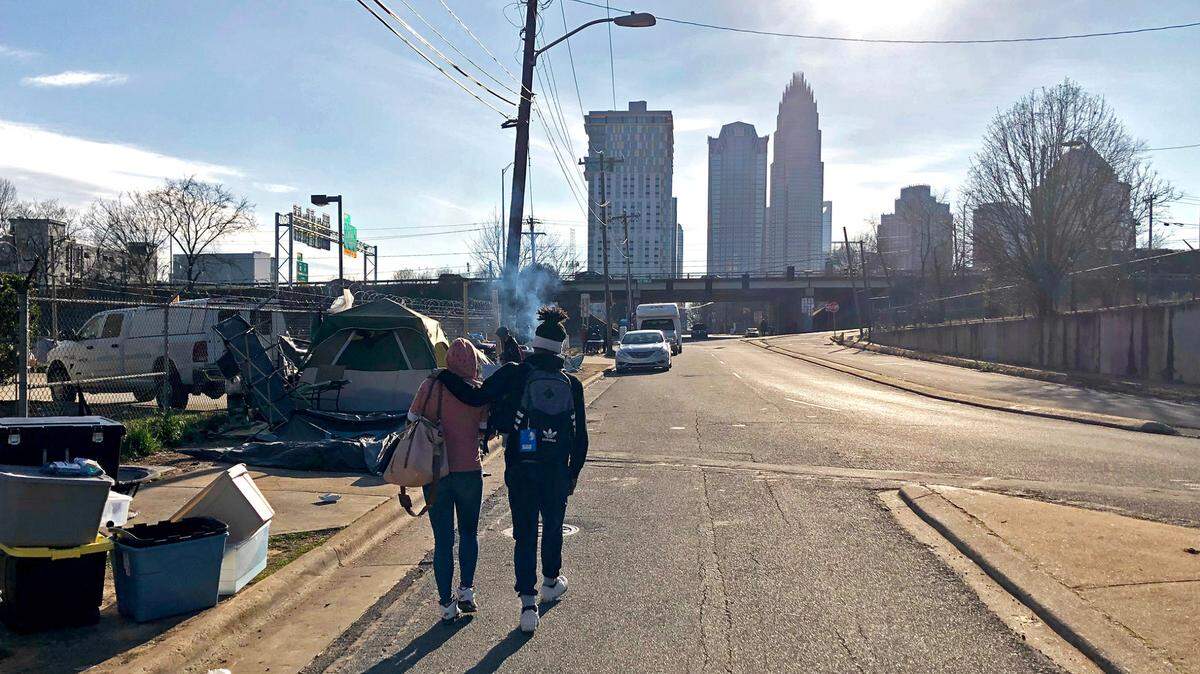 A couple walk up the street near a now-closed homeless encampment in Charlotte, on Feb. 18, 2021. 