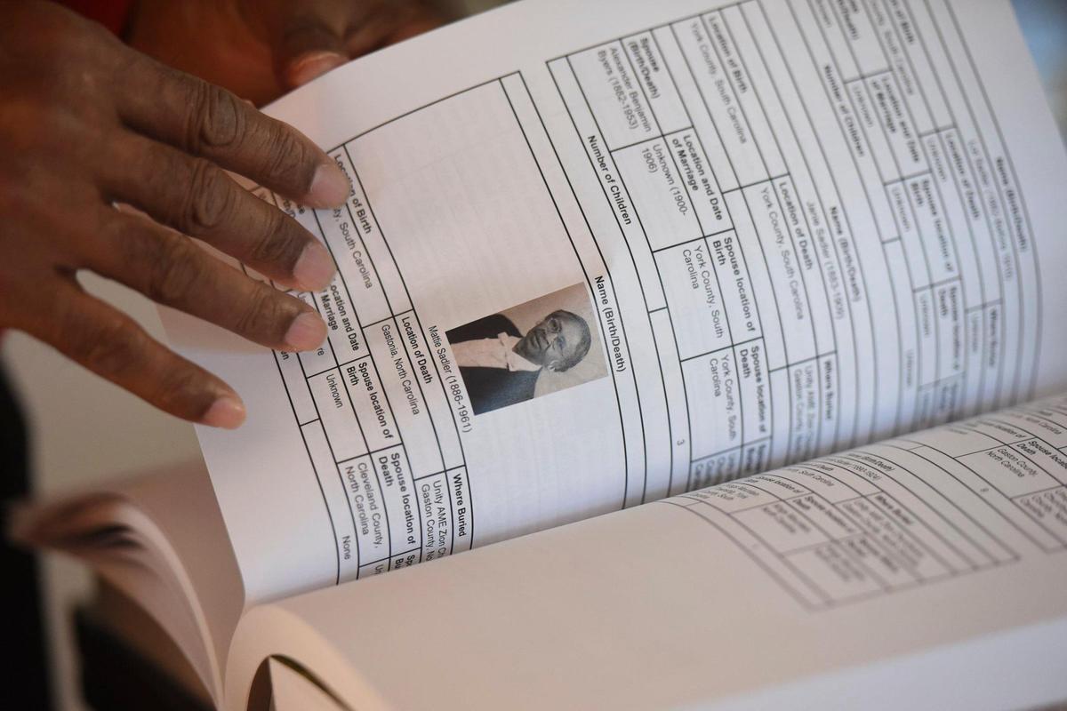 John Sadler, of Charlotte, N.C. shows pages of his book “The Road to Freedom” containing images and histories of family at his home in Charlotte, N.C. Friday, Feb. 11, 2022.