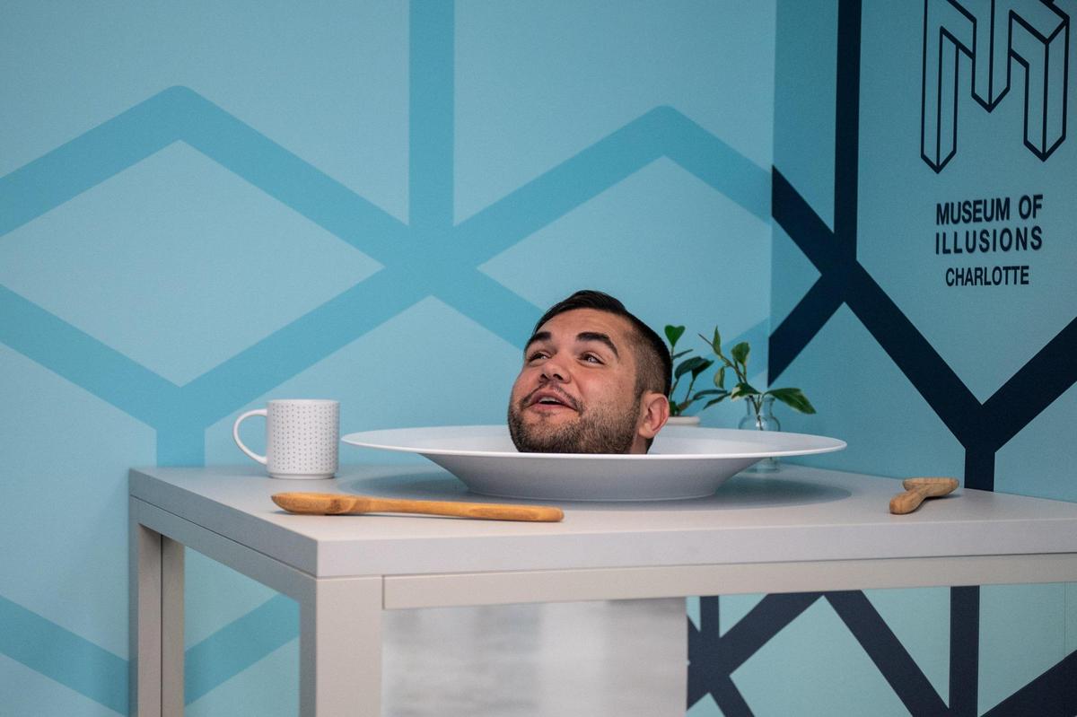 Curtis Groll sticks his head into the head on a platter installation at the grand opening ceremony for Museum of Illusions Charlotte on Tuesday, Dec. 6.