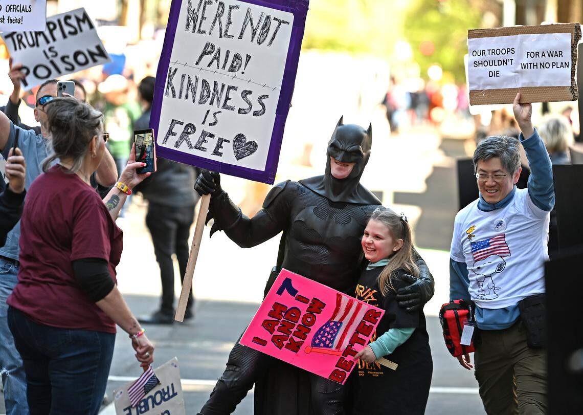 A young protester, center, poses for a photograph with Batman of Charlotte on North Tryon Street on March 28 at a No Kings rally.