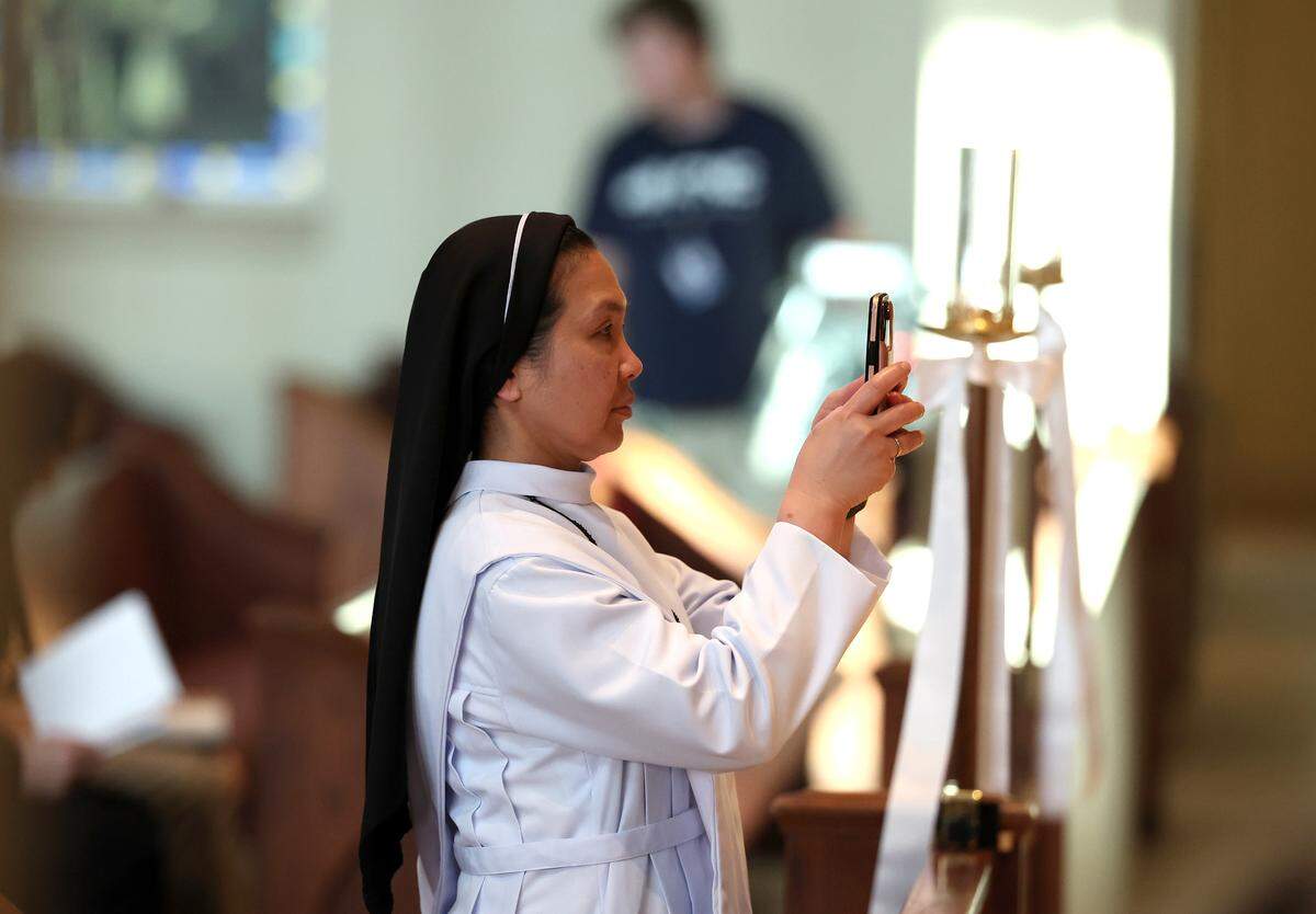 A nun takes a photograph of the altar covered in flowers and a photo of deceased Pope Francis prior to a Mass on Wednesday at Saint Mark Catholic Church in Huntersville.