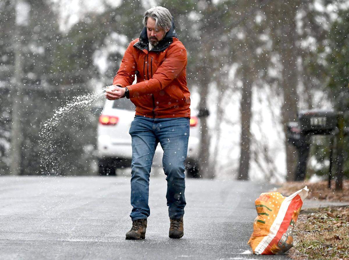 Snow falls as Charlie Weeks spreads salt onto the hill leading up into his Wilby Drive neighborhood in Charlotte, NC on Friday, January 10, 2025.