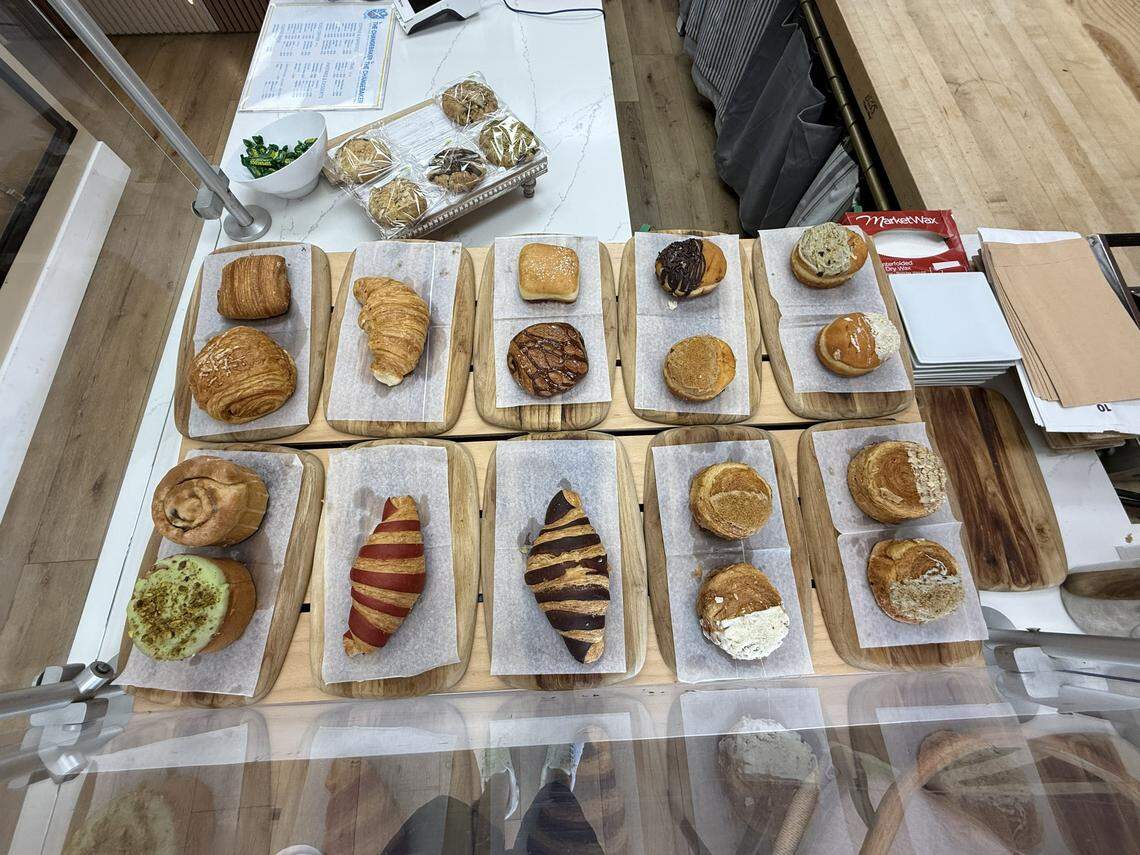 A top-down view of a bakery display featuring a variety of artisanal pastries on wooden boards. Selections include plain and chocolate-drizzled croissants, pistachio-topped rolls, and filled donuts.
