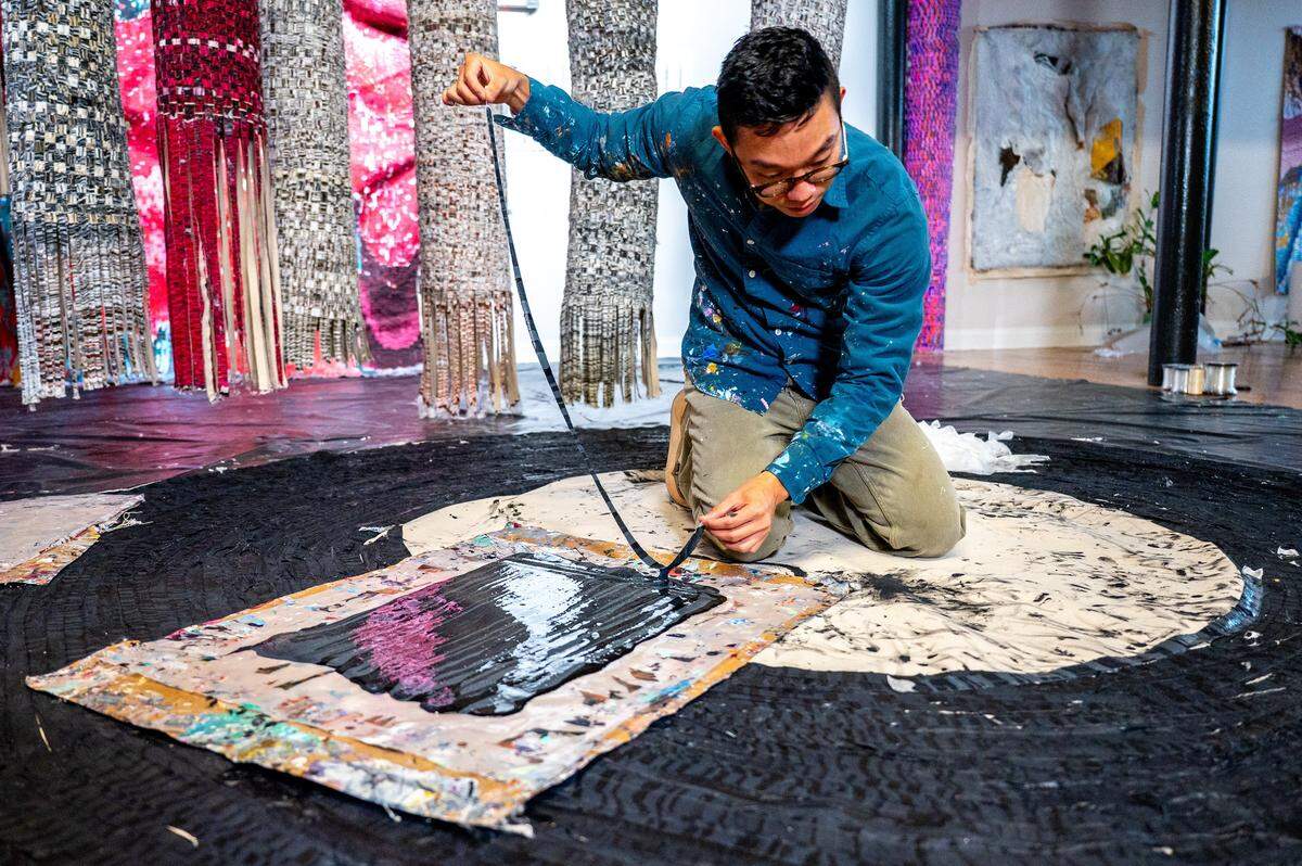 Kenny Nguyen, a Charlotte based artist, dips strips of silk into layers of paint before lying them onto of each other on a canvas in his Concord studio in Concord, NC, Tuesday August 1, 2025.