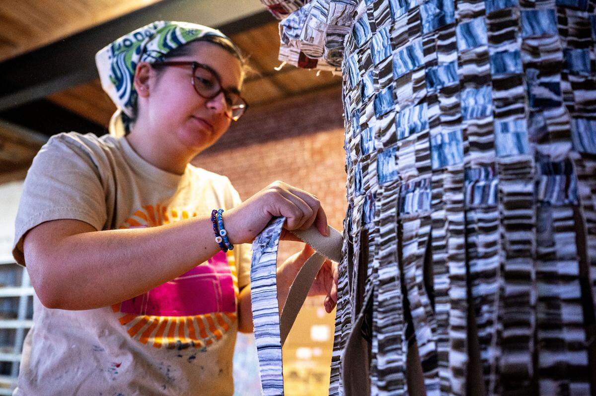 Mia Nguyen, one of Kenny Nguyen's assistants and a graduate of UNC Charlotte, weaves strips of silk dipped in paint around a plaster column in Nguyen's Concord studio in Concord, NC, Tuesday August 1, 2025.