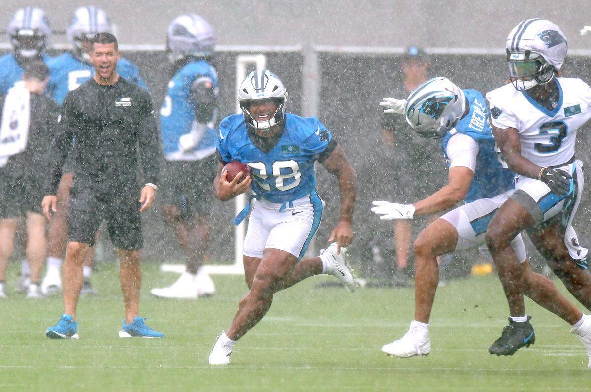 Carolina Panthers running back AJ Dillon, center, breaks to the outside on a run as head coach Dave Canales, left, smiles in the background during the team's first open workout on Tuesday, May 26, 2026.