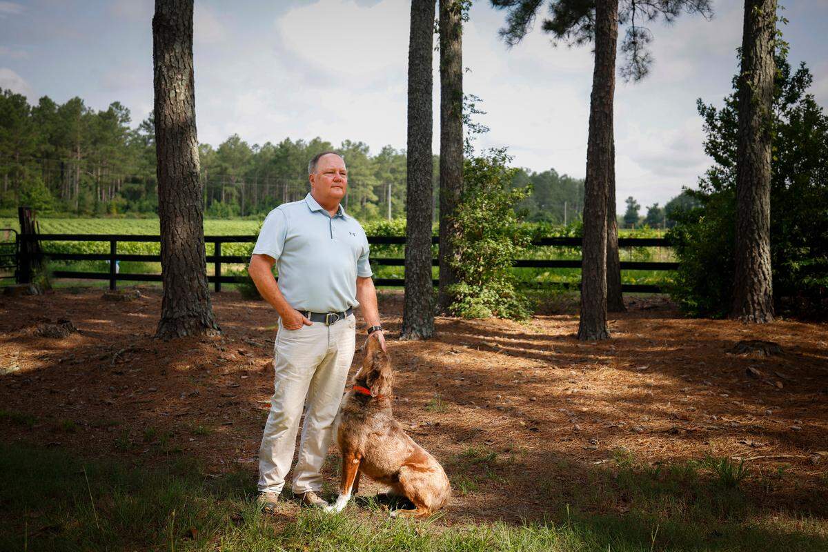 Eddie Huntley pets his dog, Levi, outside their Anson County home. Dozens of poultry barns have sprouted up near his home in recent years, bringing flies, vultures and a “really offensive” odor, he said.