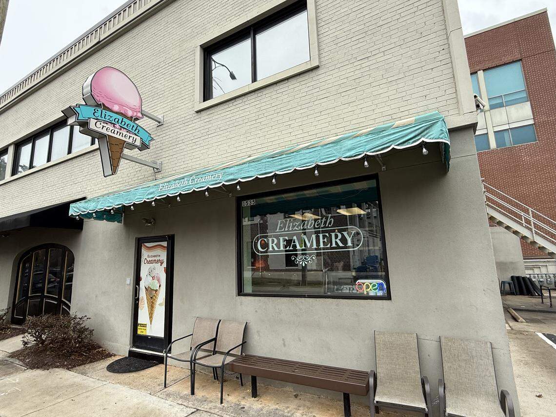Exterior of Elizabeth Creamery, a light gray building with a teal and white striped awning and a large neon-style sign shaped like a pink ice cream cone.