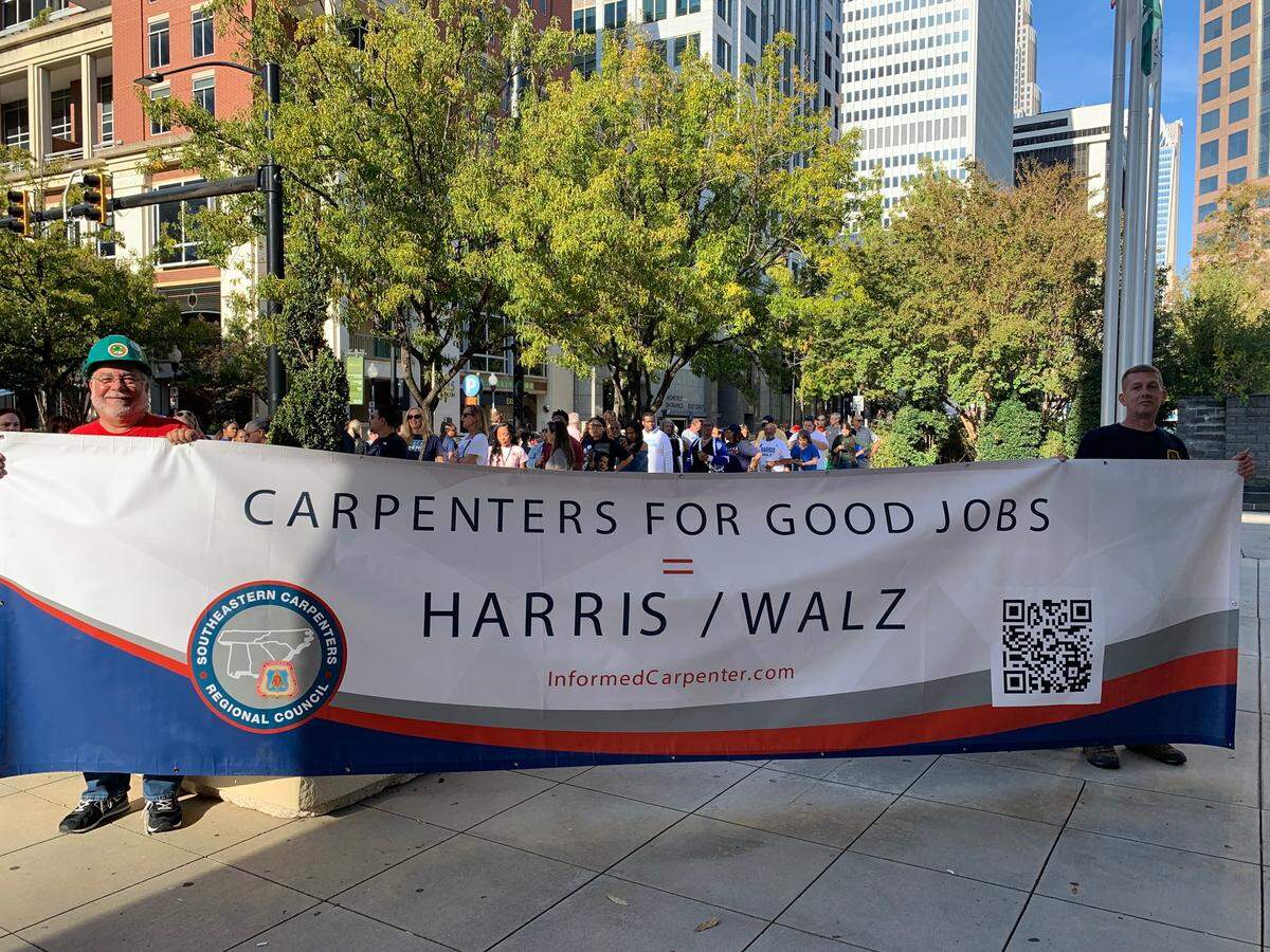 Brett Hulme, left, holds a sign touting his union’s support of Vice President Kamala Harris in the 2024 presidential election outside a campaign rally headlined by former President Barack Obama at the Charlotte Convention Center on Friday.