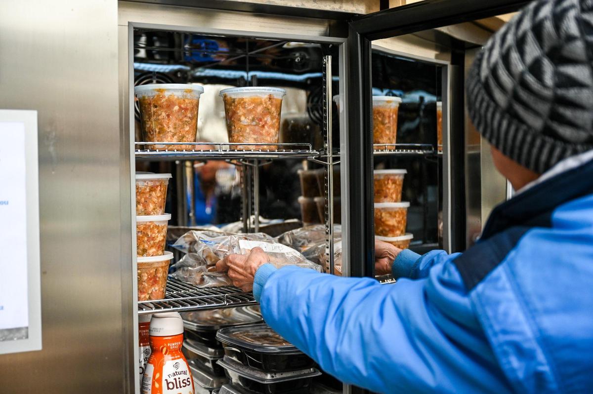 On the porch of QC Family Tree, woman reaches for a bag of hot dogs inside the Freedom Fridge, a service that provides perishable and non-perishable foods at no cost, on Tuesday, January 23, 2024.